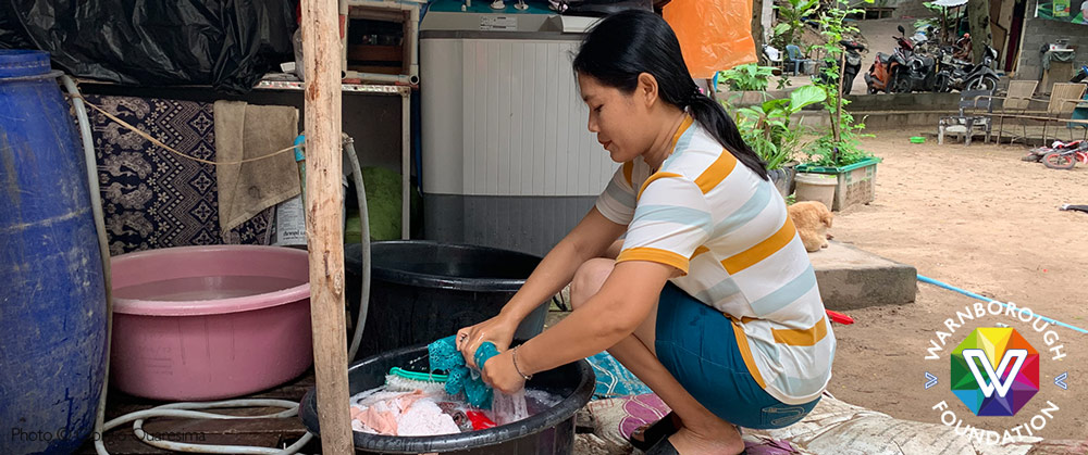 A Myanmar migrant woman washing her laundry by hand in makeshift facilities.